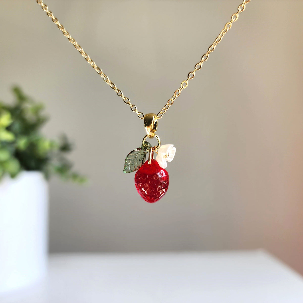 Gold strawberry charm necklace with white flower and green leaf pendant, close view
