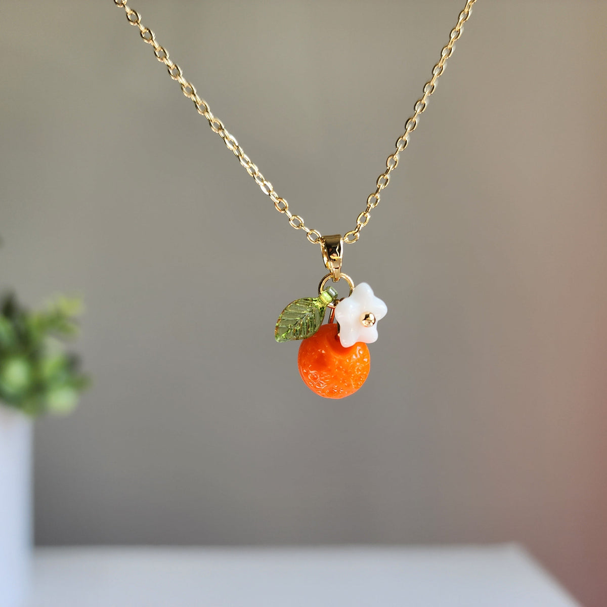 Gold-tone orange fruit charm necklace with white flower cap and green leaves
