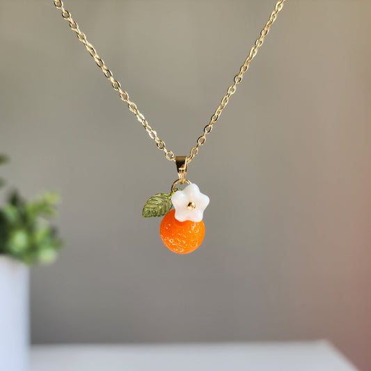 Gold-tone orange fruit and white flower charm necklace with green leaf detail