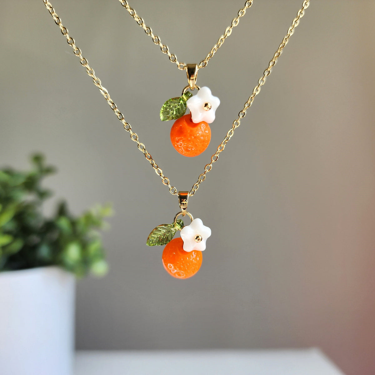 Gold-tone orange fruit charm necklace with two layered charms and green leaves