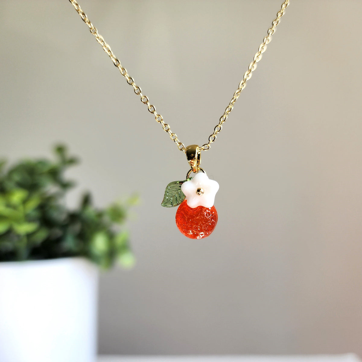Gold-tone orange fruit charm necklace with white flower and green leaf