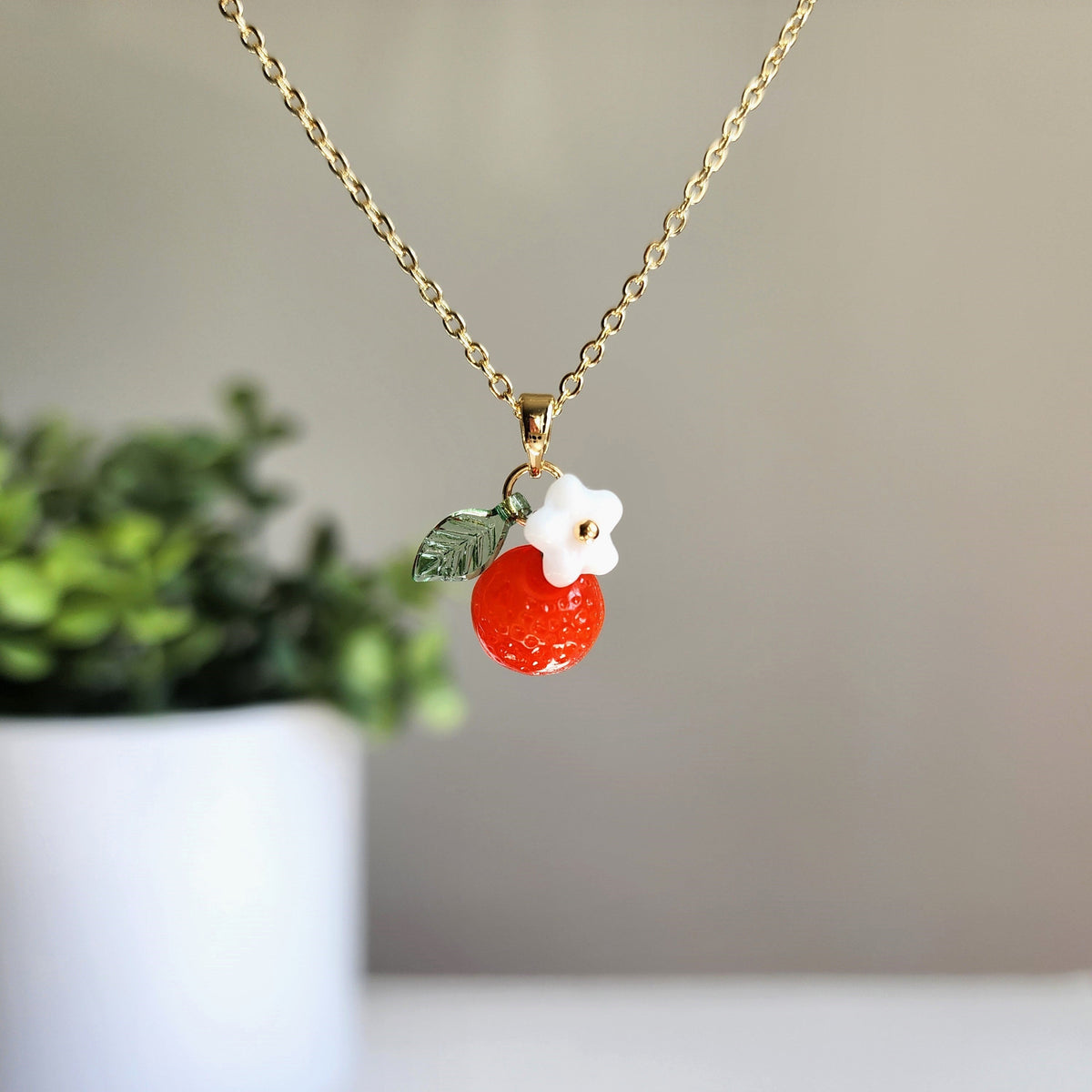 Gold-tone orange fruit charm necklace with white flower top and green leaf