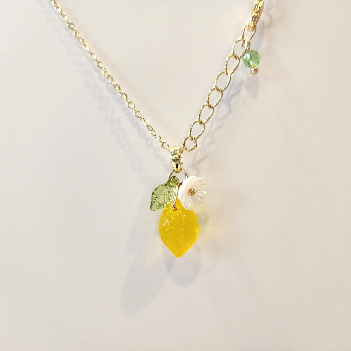 Gold chain lemon pendant necklace with yellow charm, white flower, and green leaf