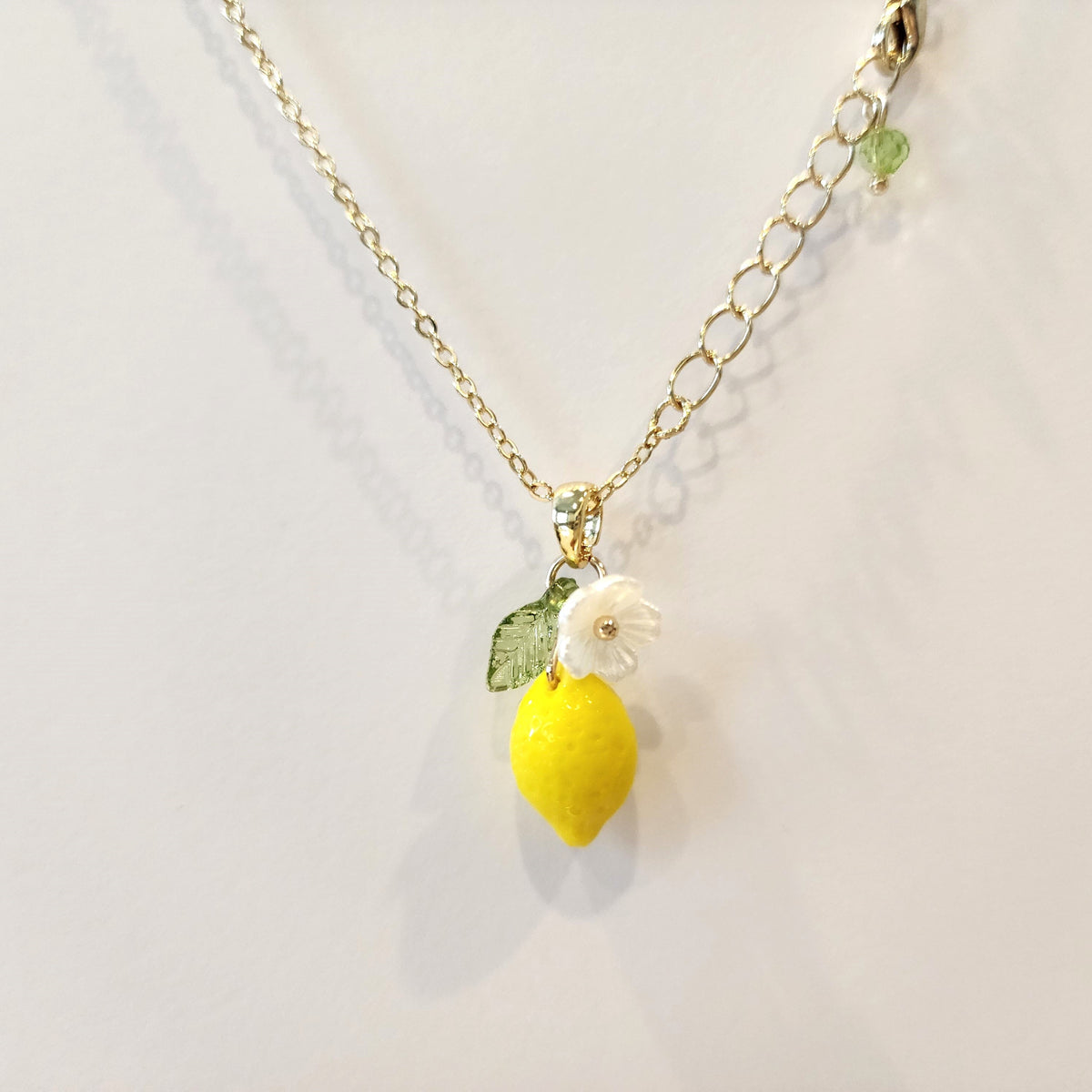 Gold chain lemon pendant necklace with yellow lemon charm, white flower, and green leaf