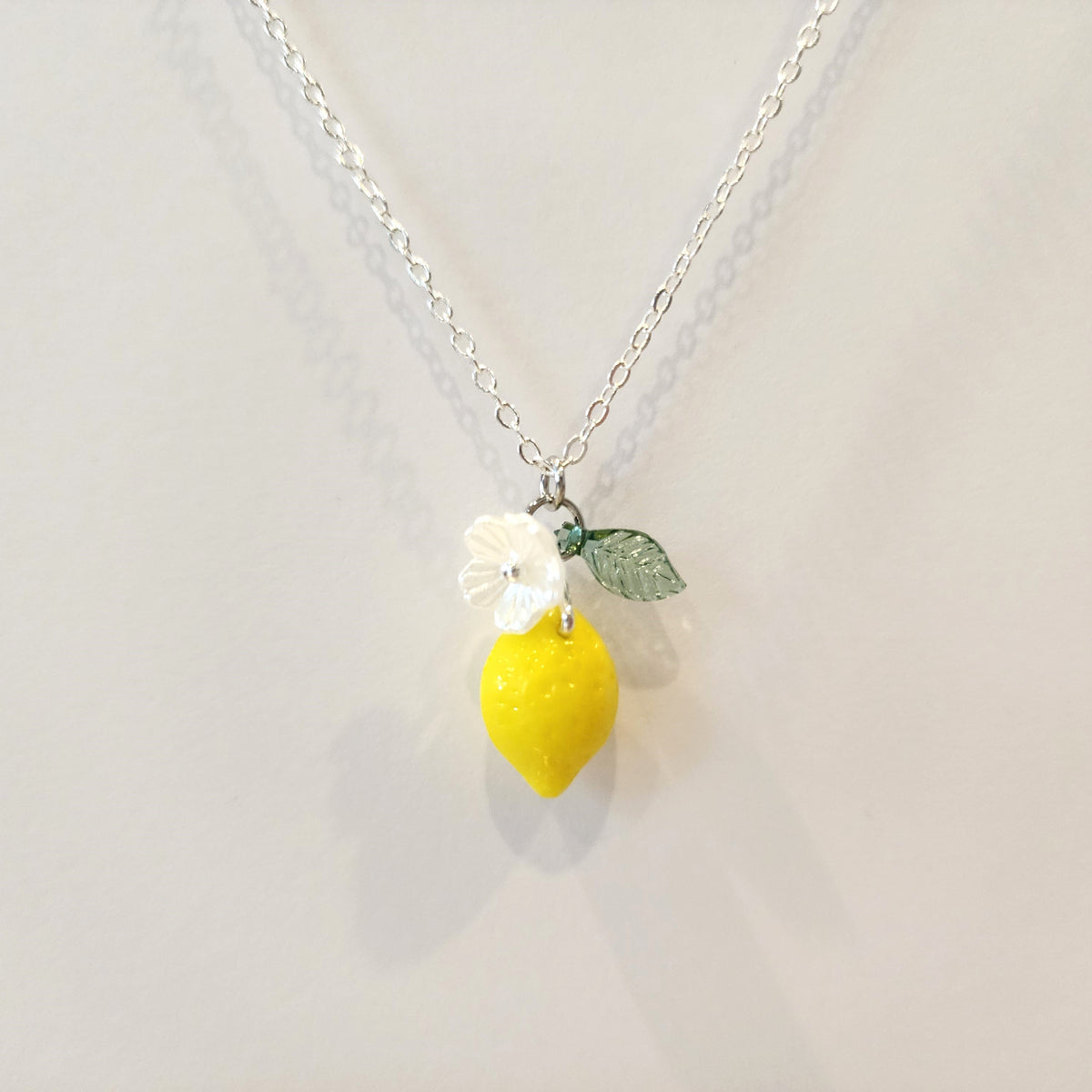 Silver chain lemon pendant necklace with yellow lemon, white flower, and green leaf