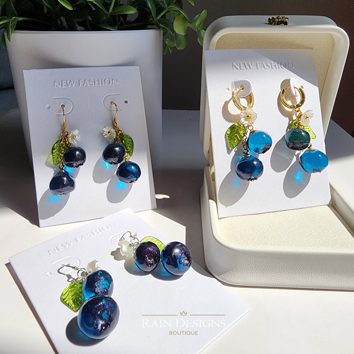 Blueberry cluster dangle earrings with blue resin berries and green leaves on retail cards