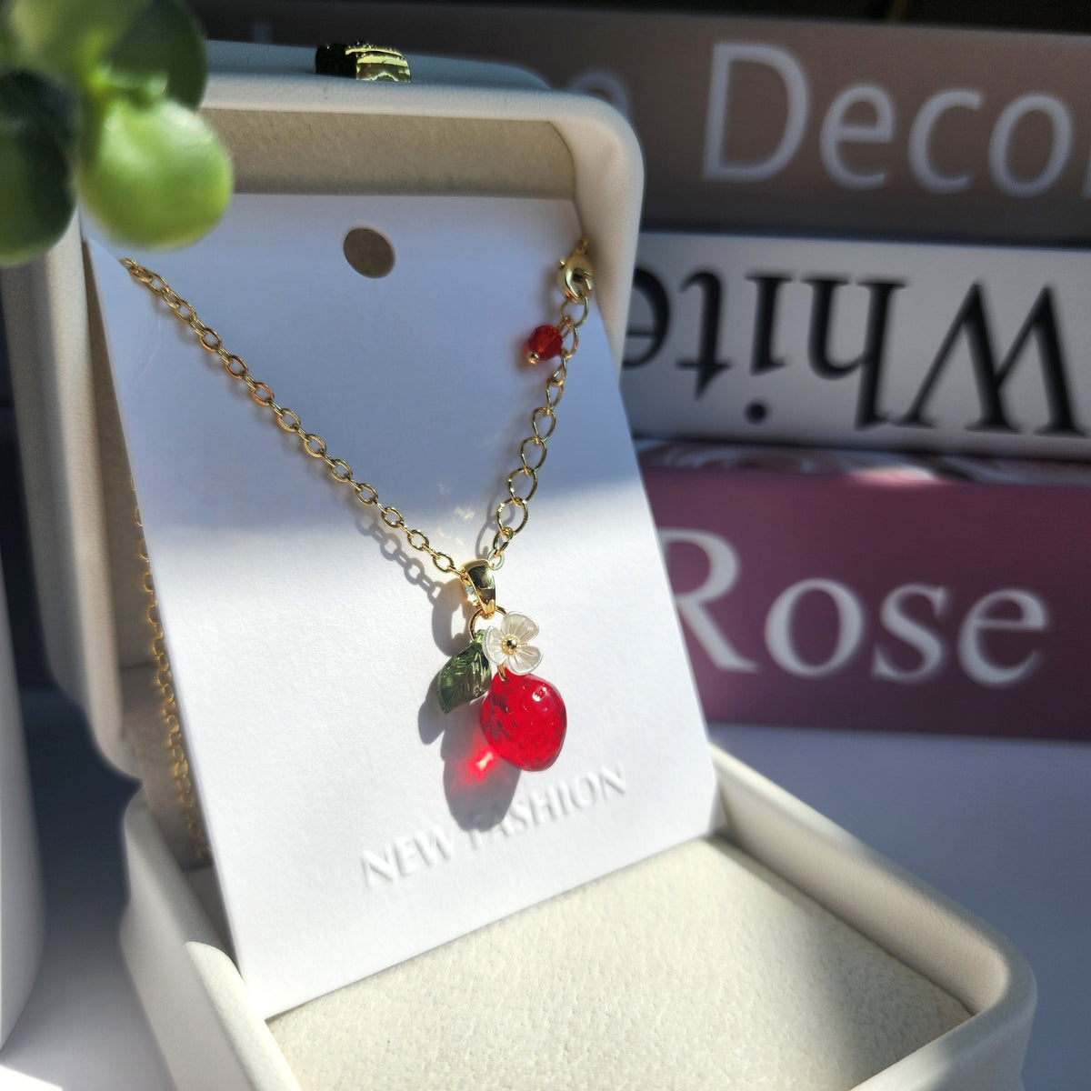 Gold strawberry pendant necklace with white blossom and green leaf charms on chain