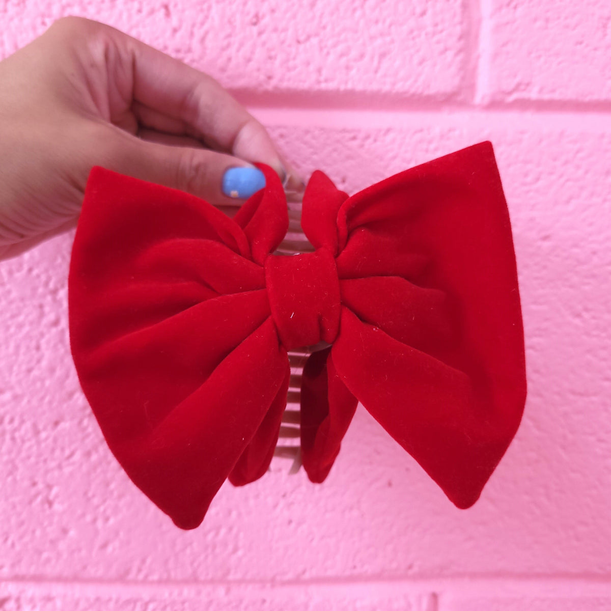 Red fabric bow hair claw with comb clip, held against pink wall