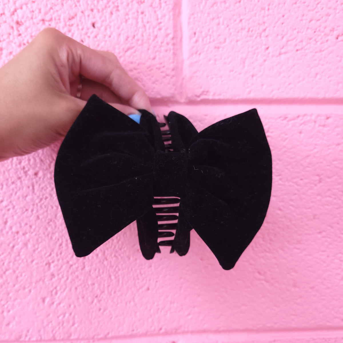 Black fabric bow hair claw with comb clip, held up for display
