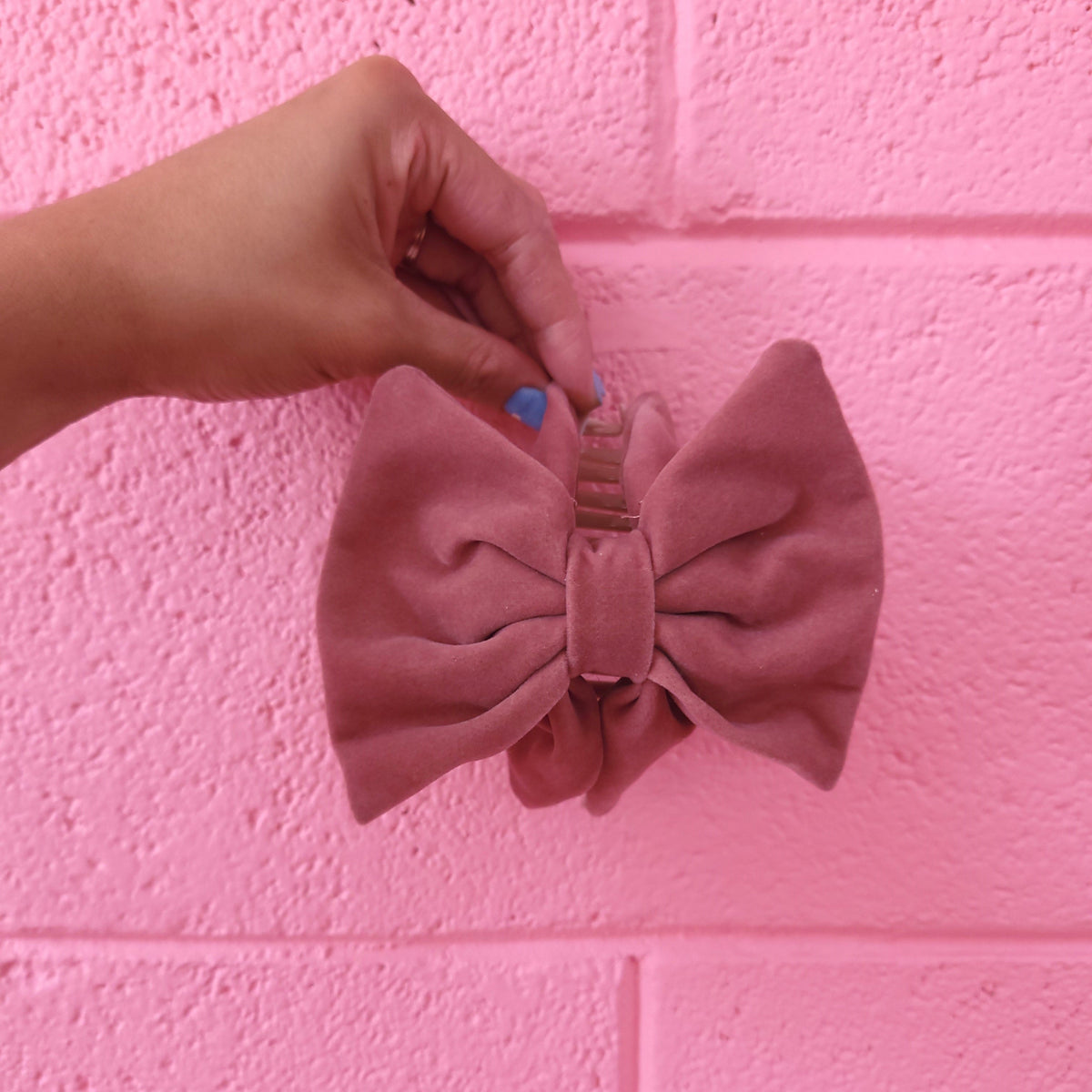 Light pink fabric bow hair claw with comb clip, held up for display