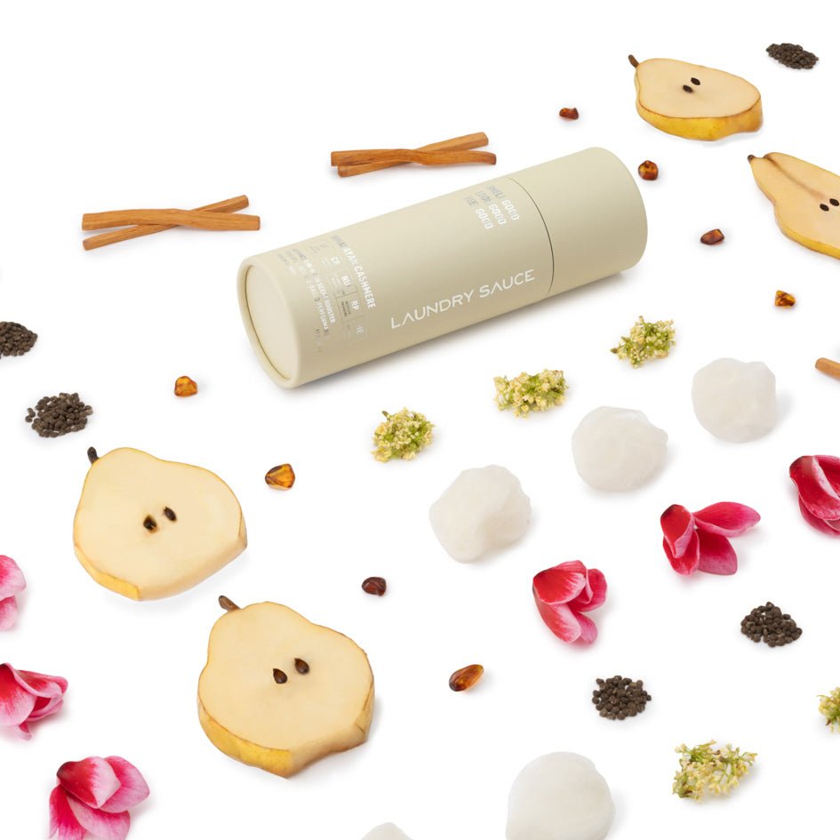Laundry scent booster tube, cream color, shown lying with scattered scented ingredients