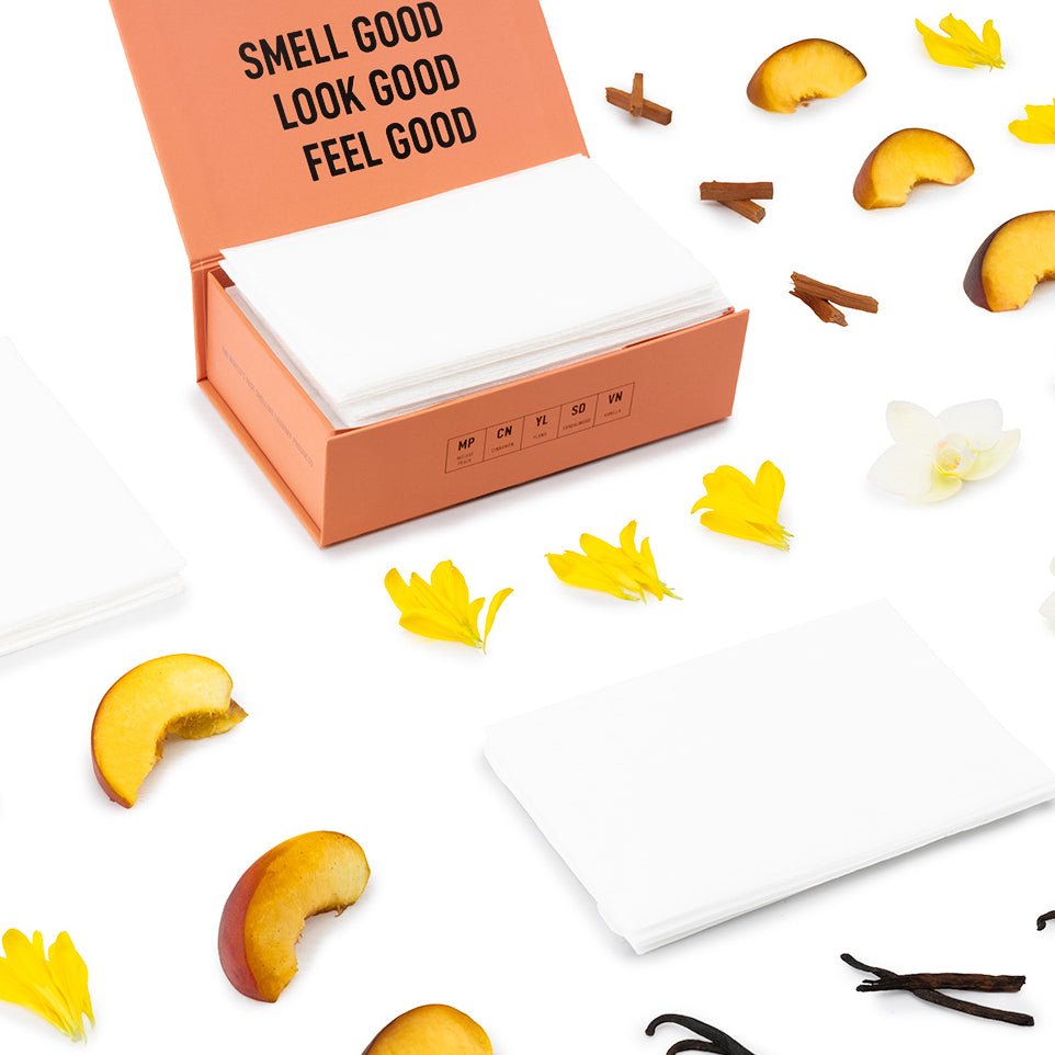 Scented dryer sheets in an orange open box with white sheets and scattered scent items