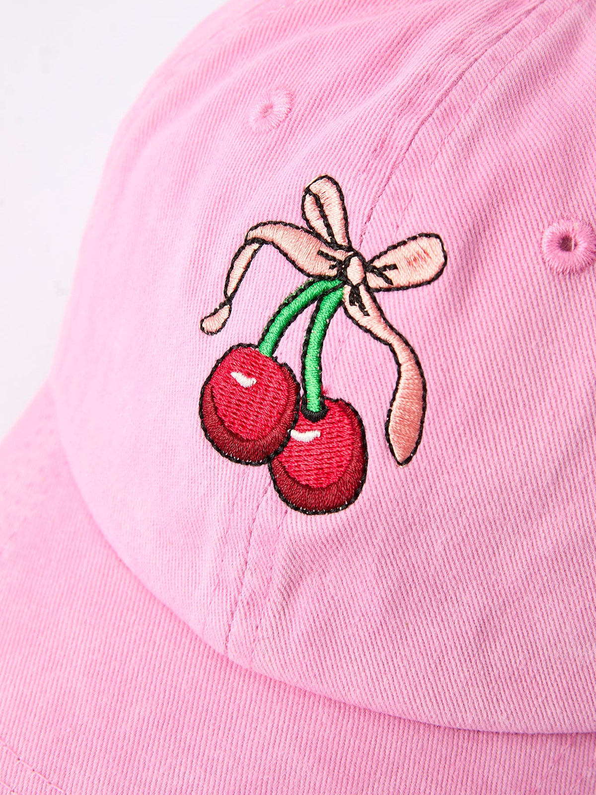 Pink girls cap close-up with embroidered cherries and bow at the front