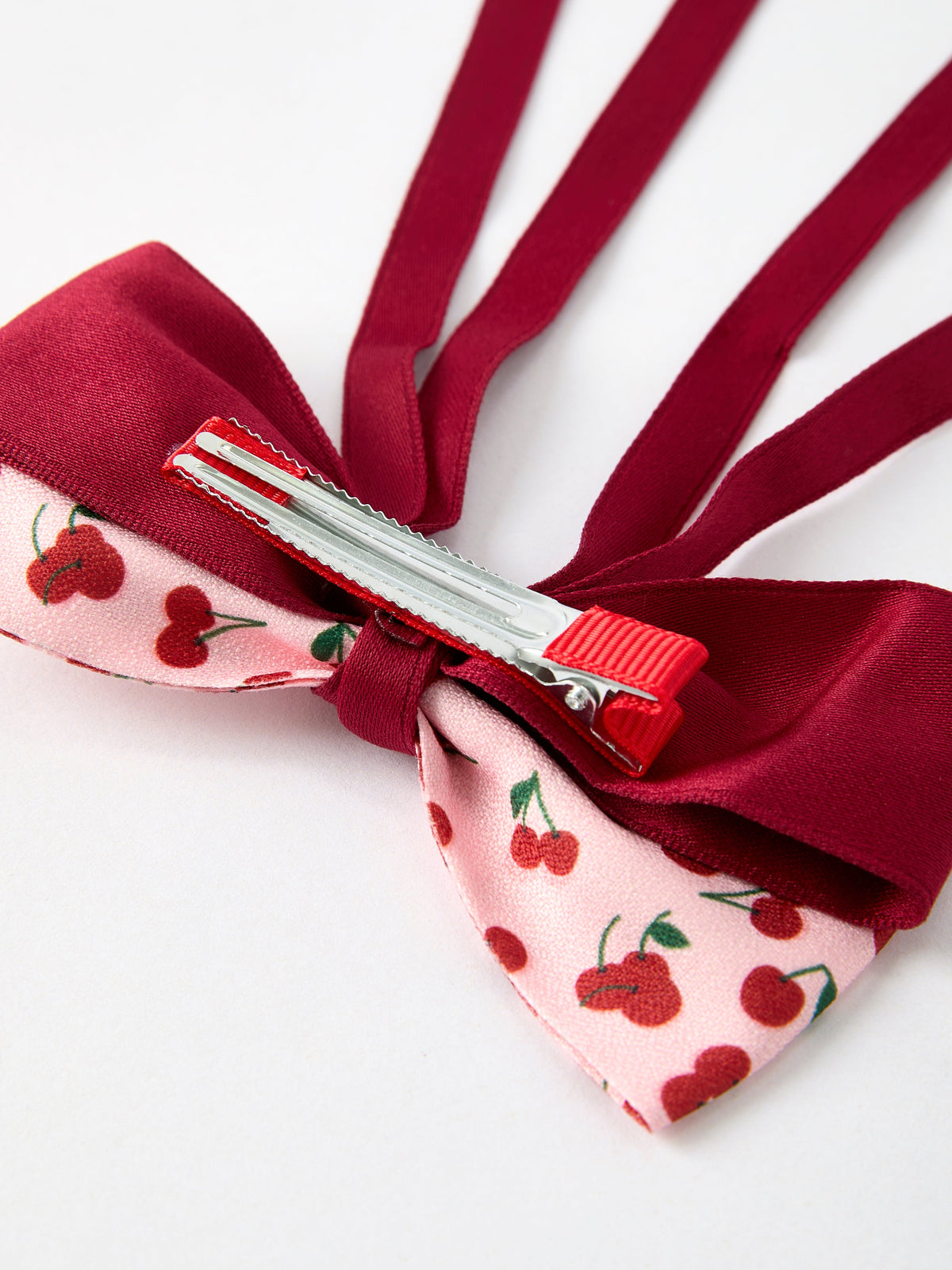 Close-up cherry bow hairpin with red ribbon, silver pin, and metal clasp