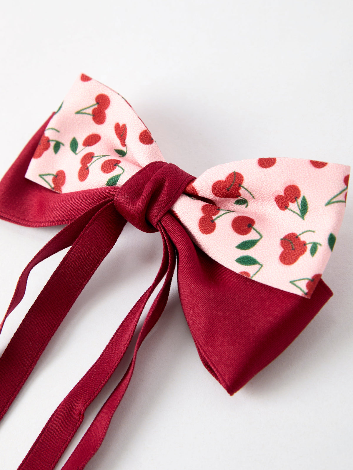 Cherry-pattern fabric bow with burgundy ribbon tails on a hairpin clip