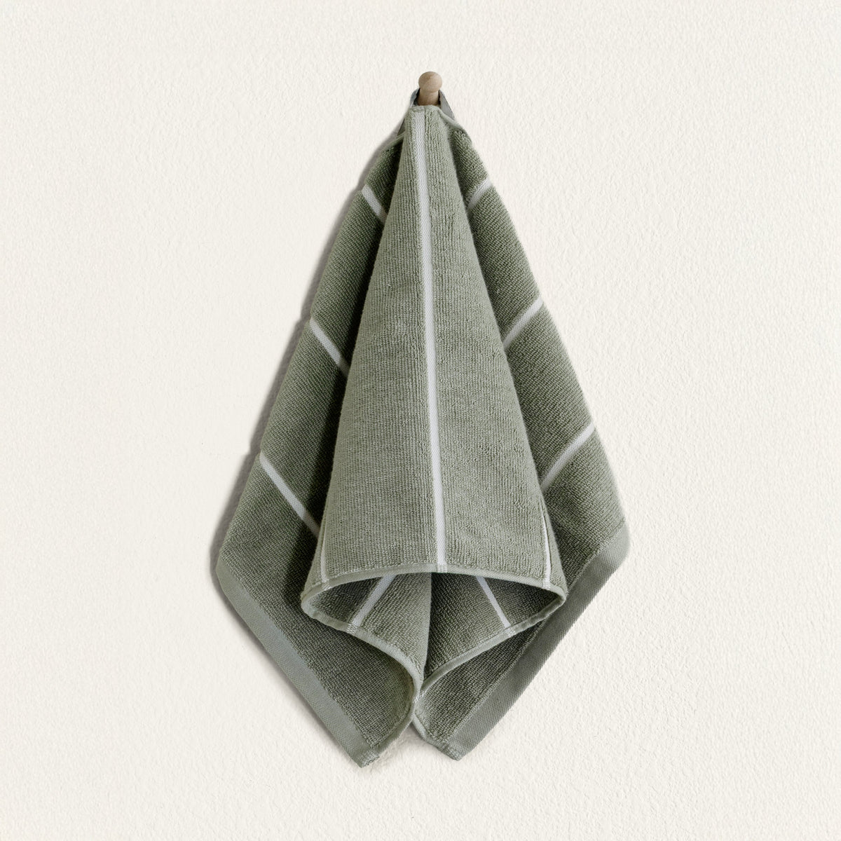 Sage green cotton hand towel with white border detail, folded and hanging