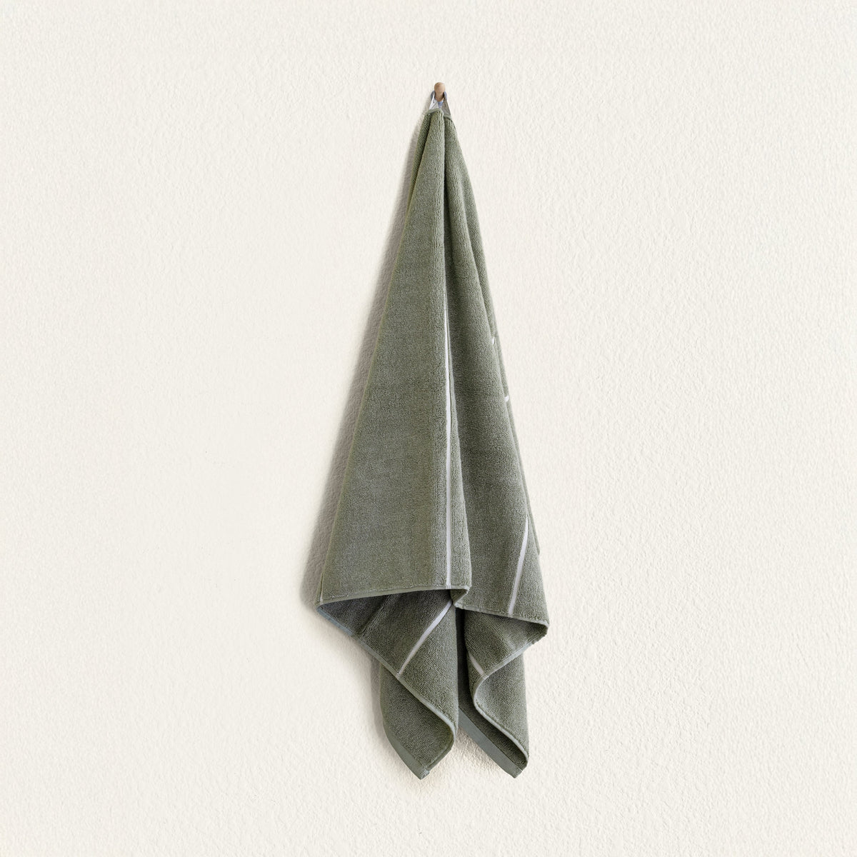 Sage green cotton towel with white edge trim, folded and hanging