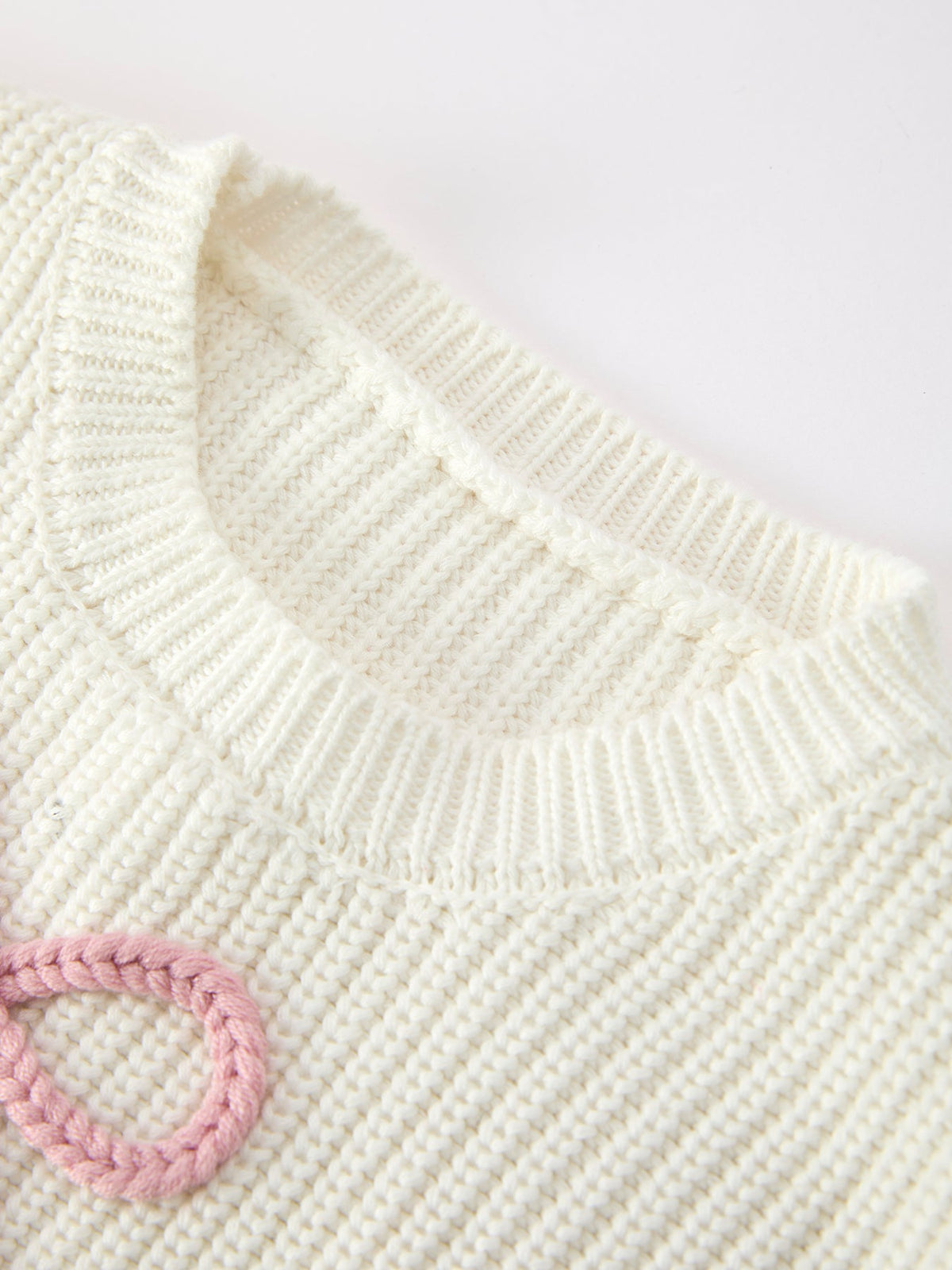 Cream knit sweater close-up: ribbed collar and pink bow over textured knit