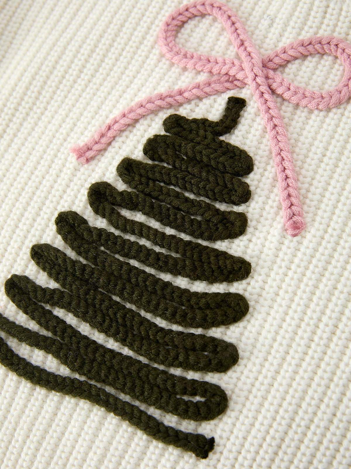Cream knit sweater close-up: dark green Christmas tree graphic with pink bow