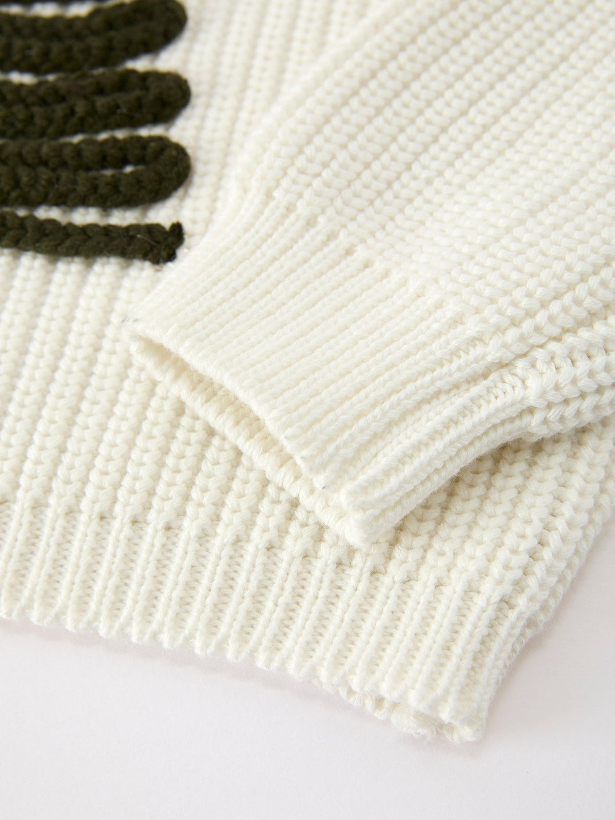 Cream knit sweater close-up of ribbed hem and cuffs with thick stitch texture