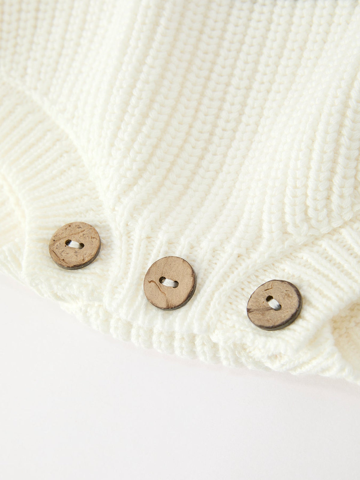 Cream knit romper hem with three wooden-look buttons and snap closure
