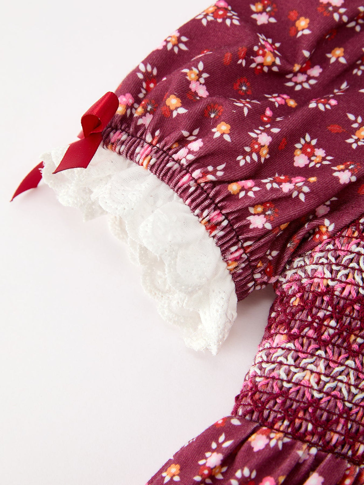 Sleeve and waist close-up: burgundy floral smocked cuff with red bow and lace