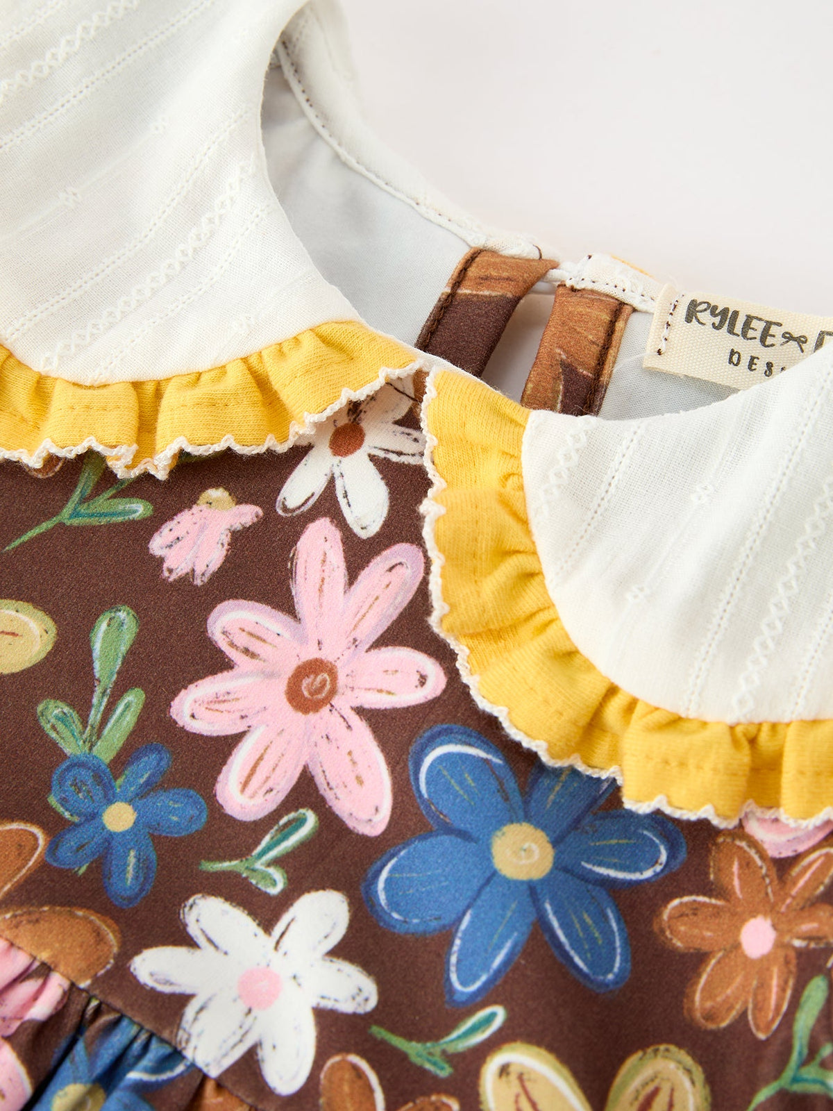 Close-up of brown floral romper neckline with white collar ruffle and yellow trim