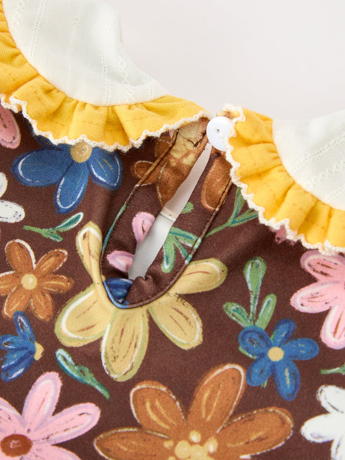 Brown floral baby romper front with white yoke, yellow ruffled trim, button placket