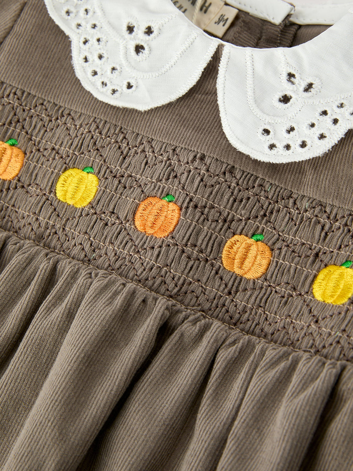 Smocked waist detail with four embroidered orange pumpkins on taupe romper
