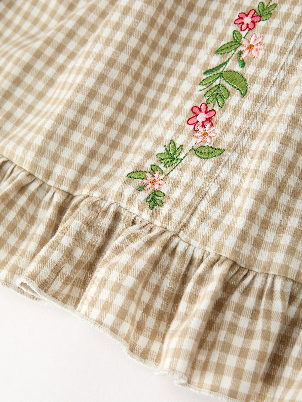 Gingham plaid girls dress with floral embroidery along the bodice and ruffled skirt hem