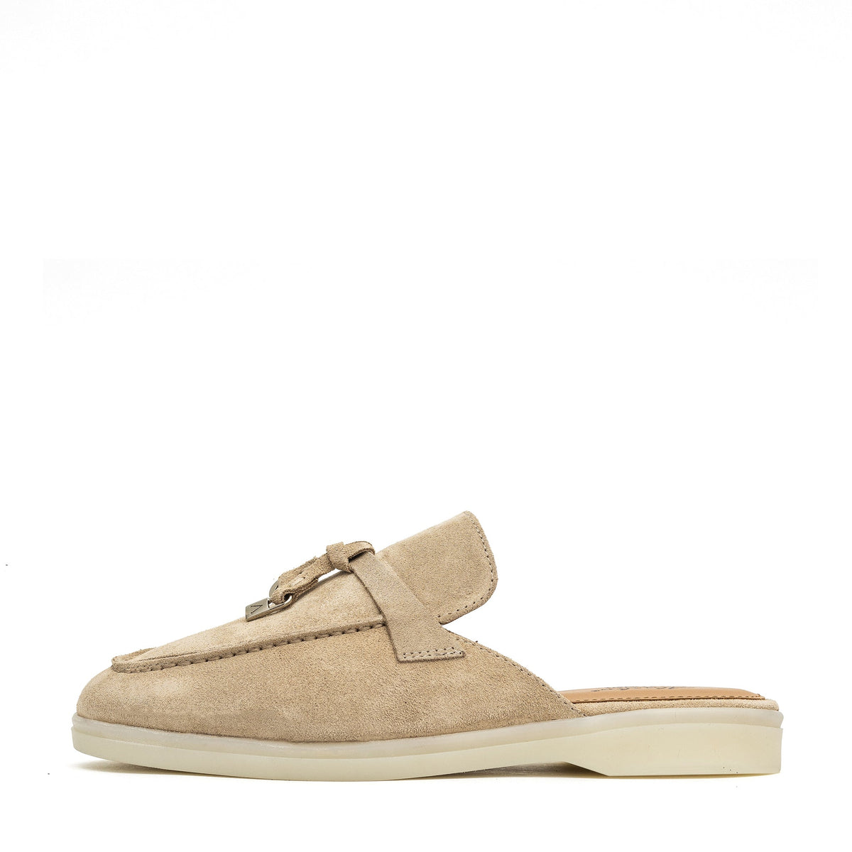 Side view of a beige suede mule with a metal charm and low cream sole