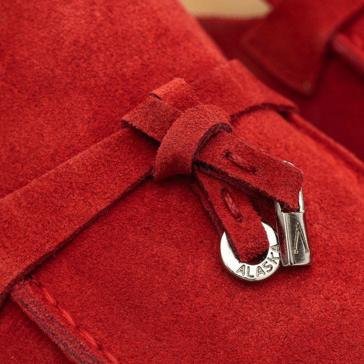 Close-up of a red suede mule's tassel detail with metal tips.
