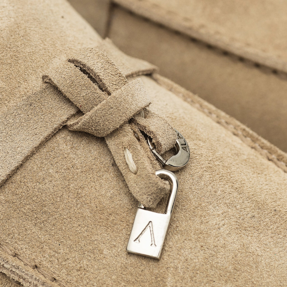 Close-up of suede strap and polished metal charm on a beige mule
