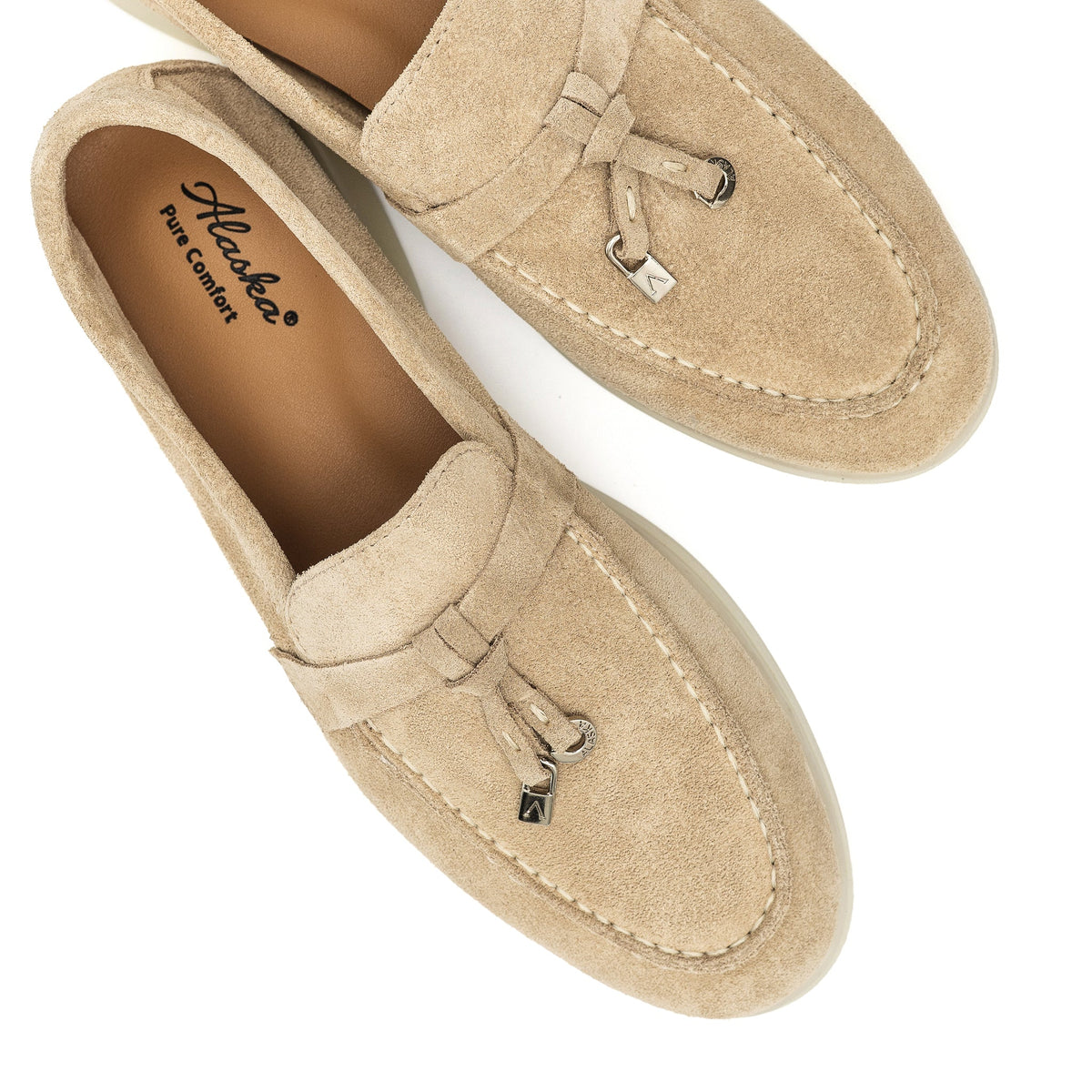 Top view of beige suede loafers with stitched aprons, metal charms, and branded insoles