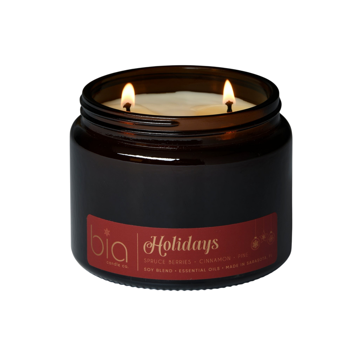 Dark amber candle jar with two lit flames and “Holidays” label
