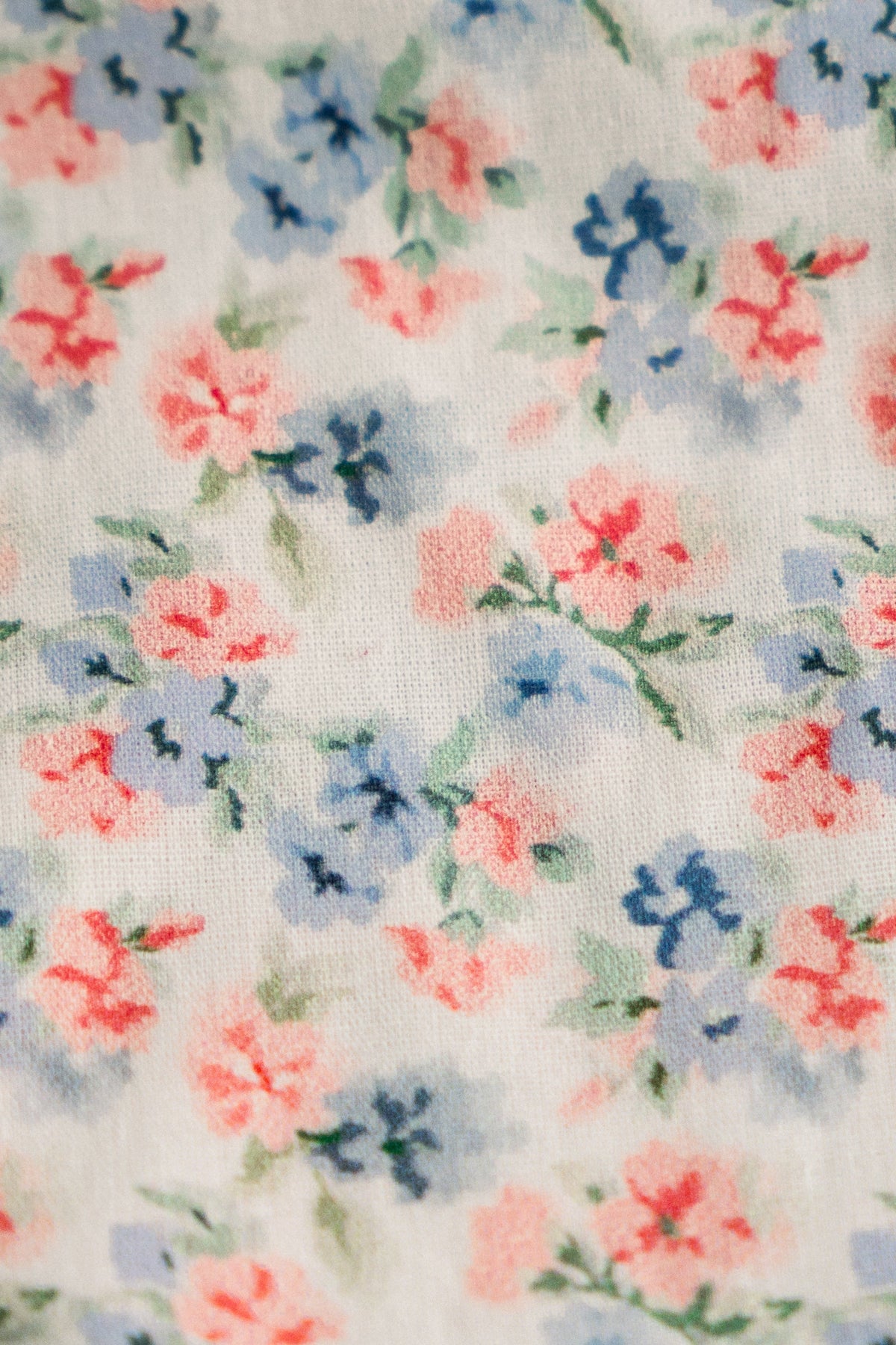 Close-up of light blue floral fabric with coral pink and blue flowers and green leaves