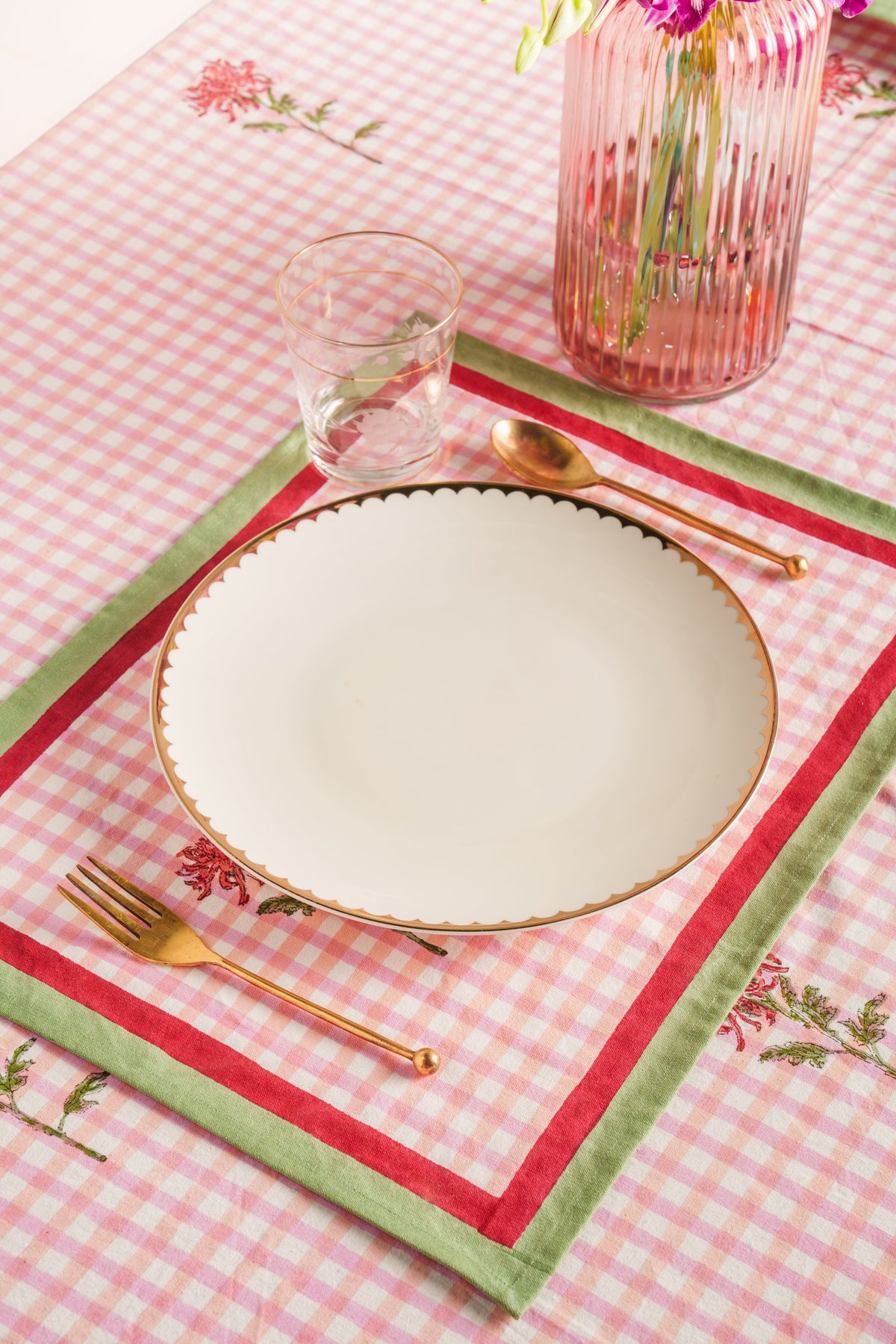 Pink gingham placemat with red floral border and green trim; empty plate and cutlery