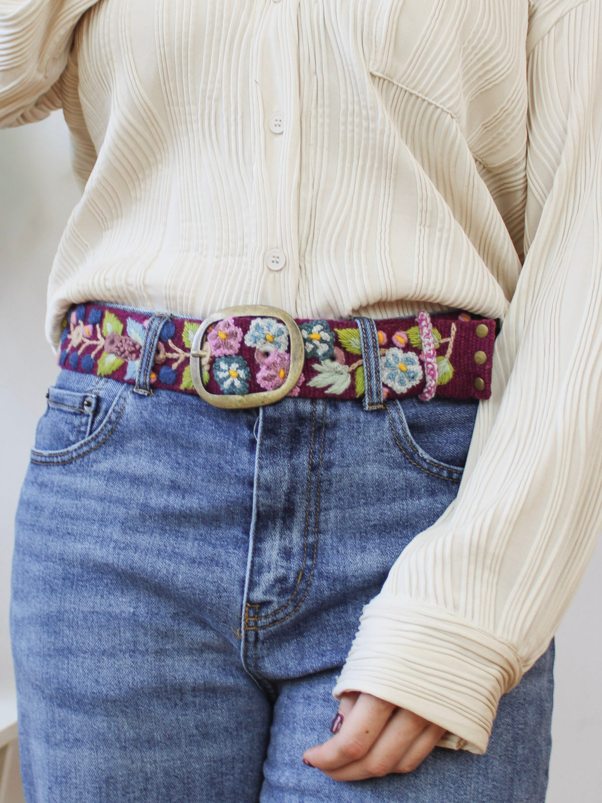 Plum embroidered wide belt with floral trim and brass buckle on denim jeans