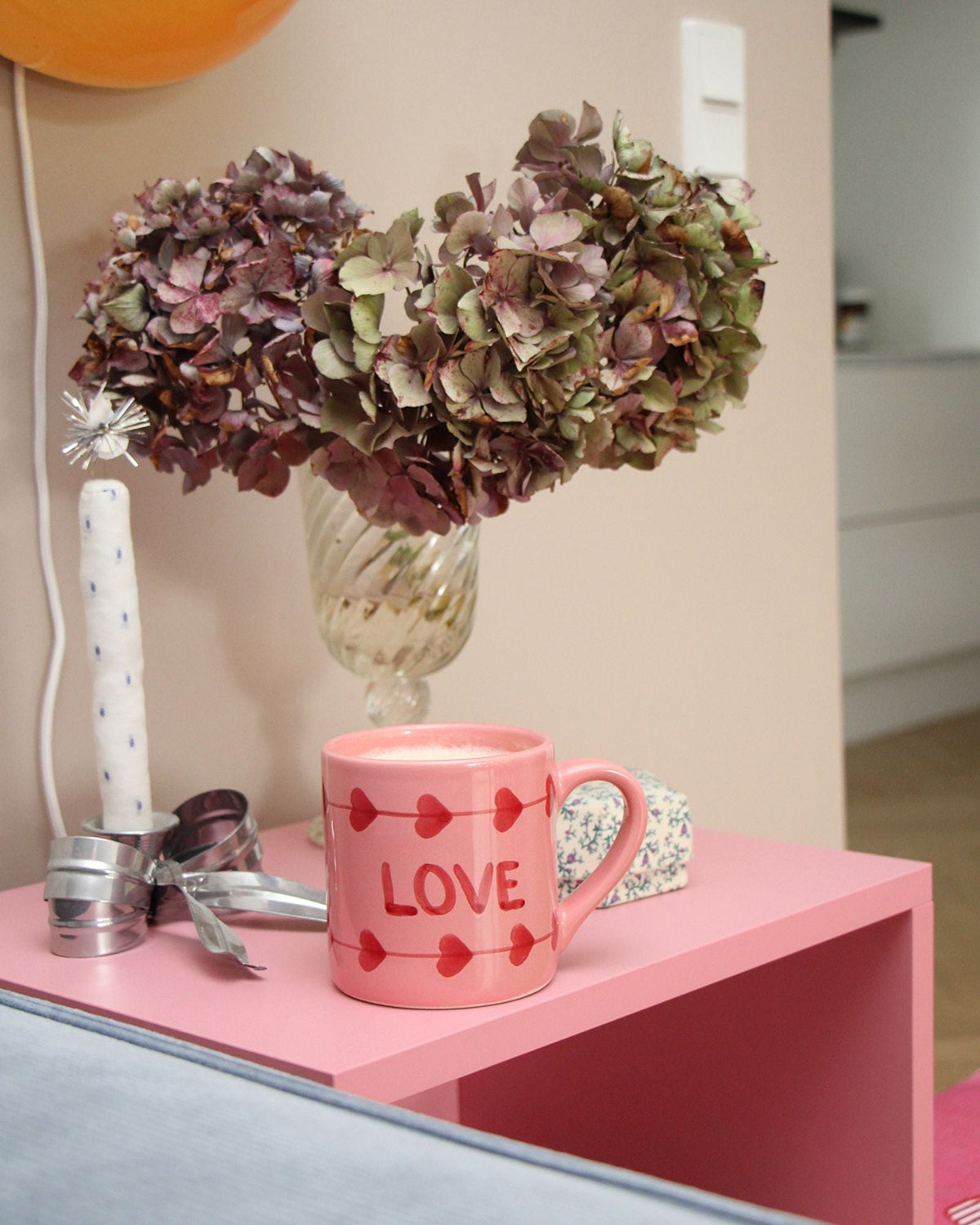 Pink ceramic mug with red hearts and 'LOVE' print, shown on a tabletop