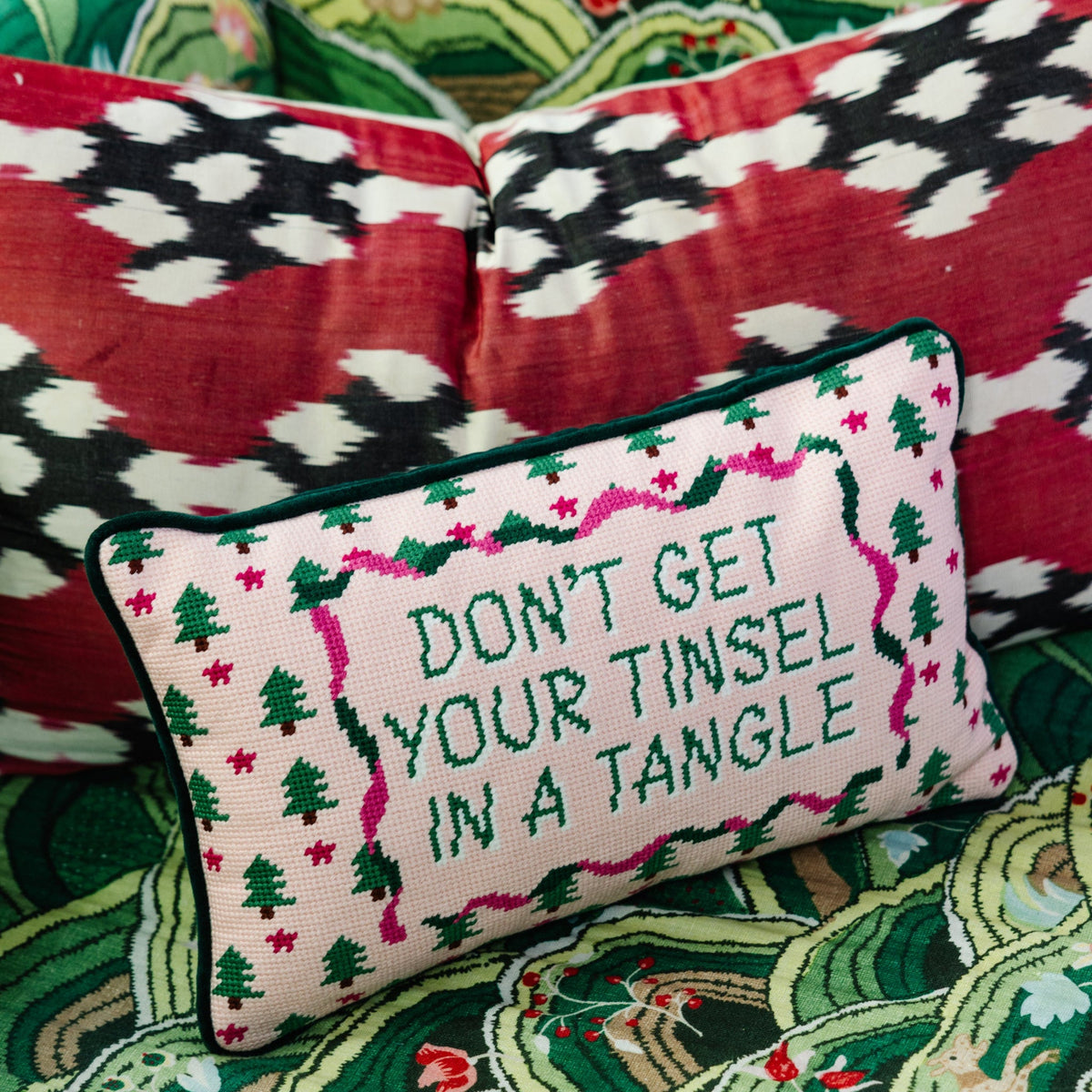 Rectangular needlepoint pillow, pink background with green trees and embroidered "DON’T GET TINSEL"