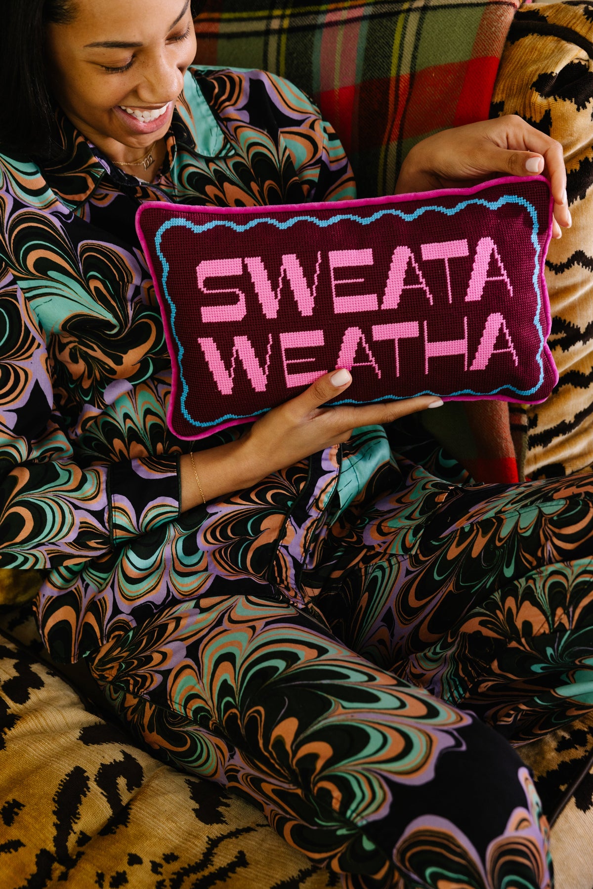 Needlepoint lumbar pillow with 'SWEATA WEATHA' lettering in purple and pink