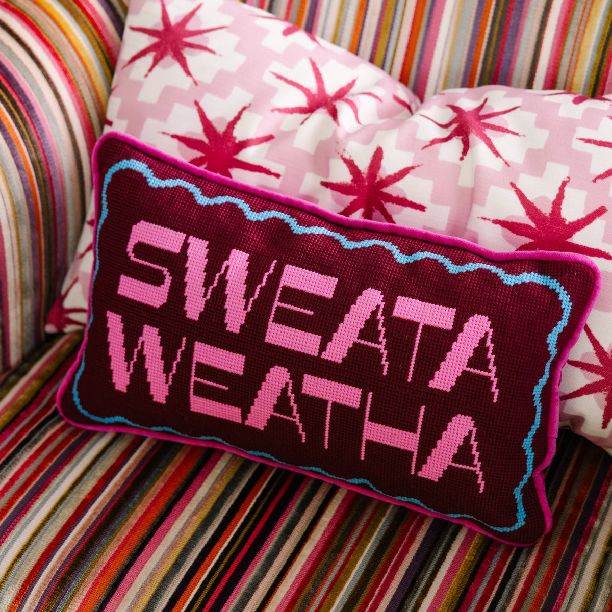 Purple needlepoint pillow with 'SWEATA WEATHA' text and blue/pink border