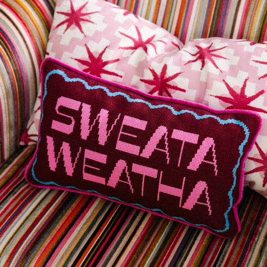Purple needlepoint pillow with 'SWEATA WEATHA' text and blue/pink border