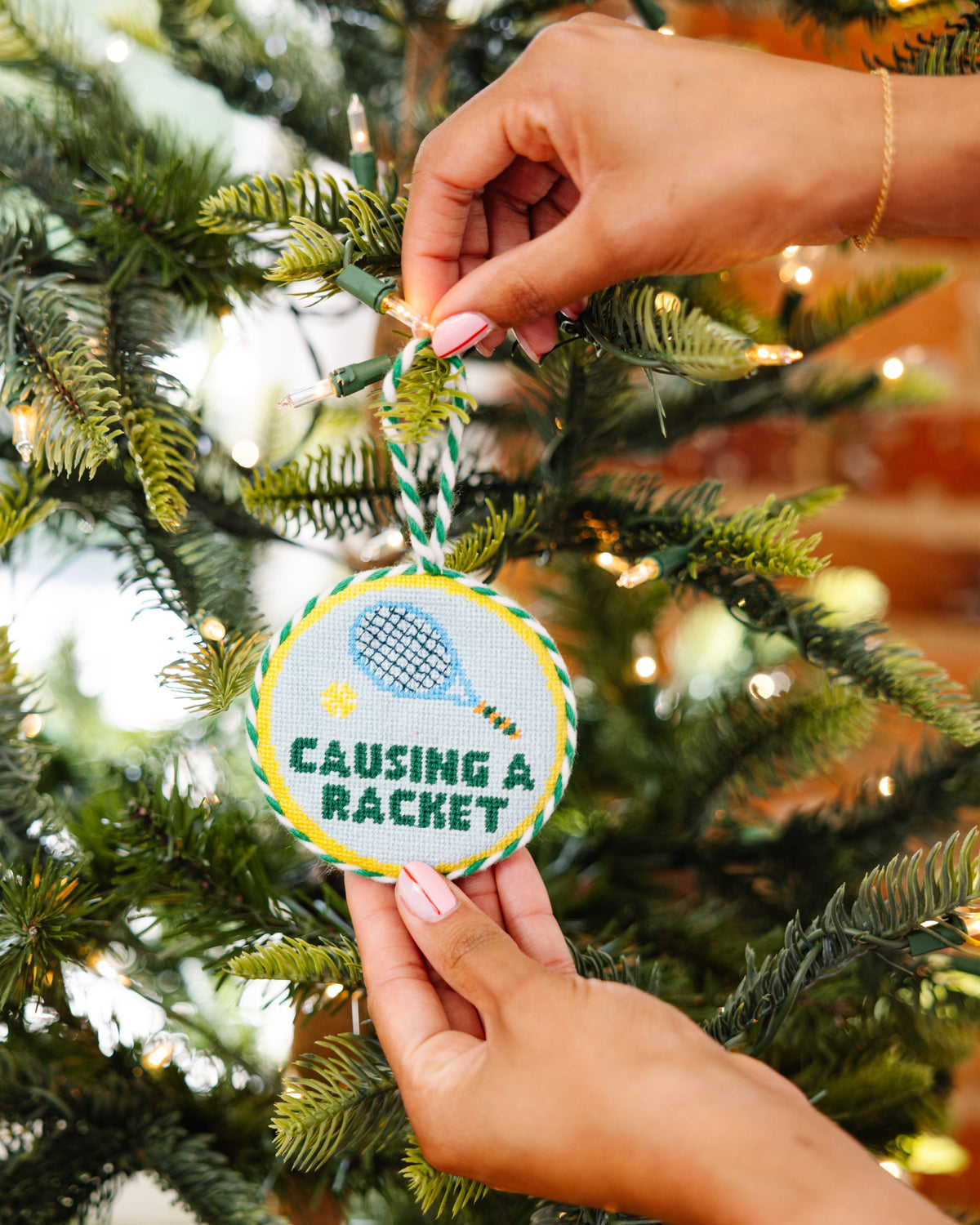 Round needlepoint Christmas ornament with blue bird design and green-and-white striped hanging cord
