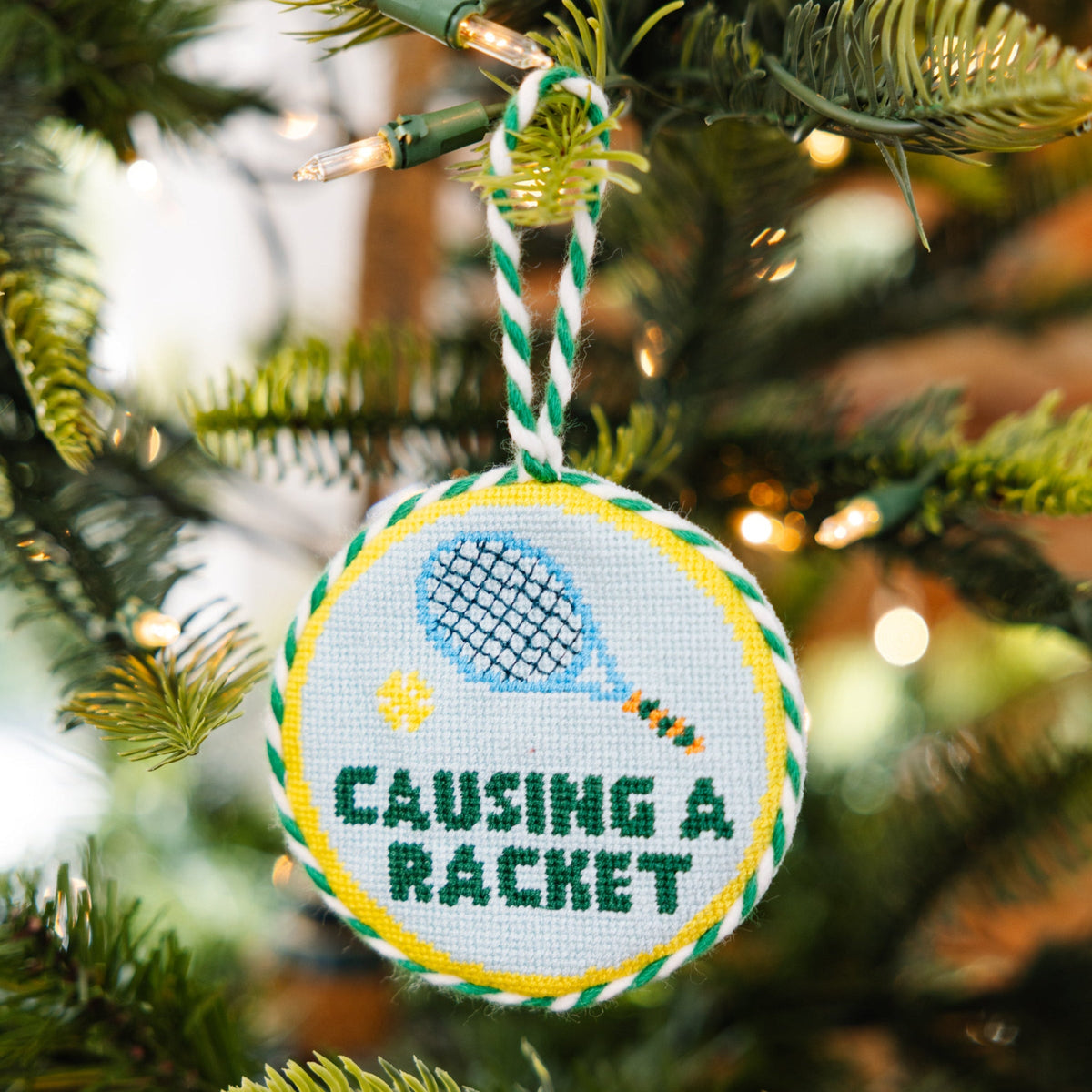 Round needlepoint Christmas ornament with blue bird, yellow details, and striped hanging loop