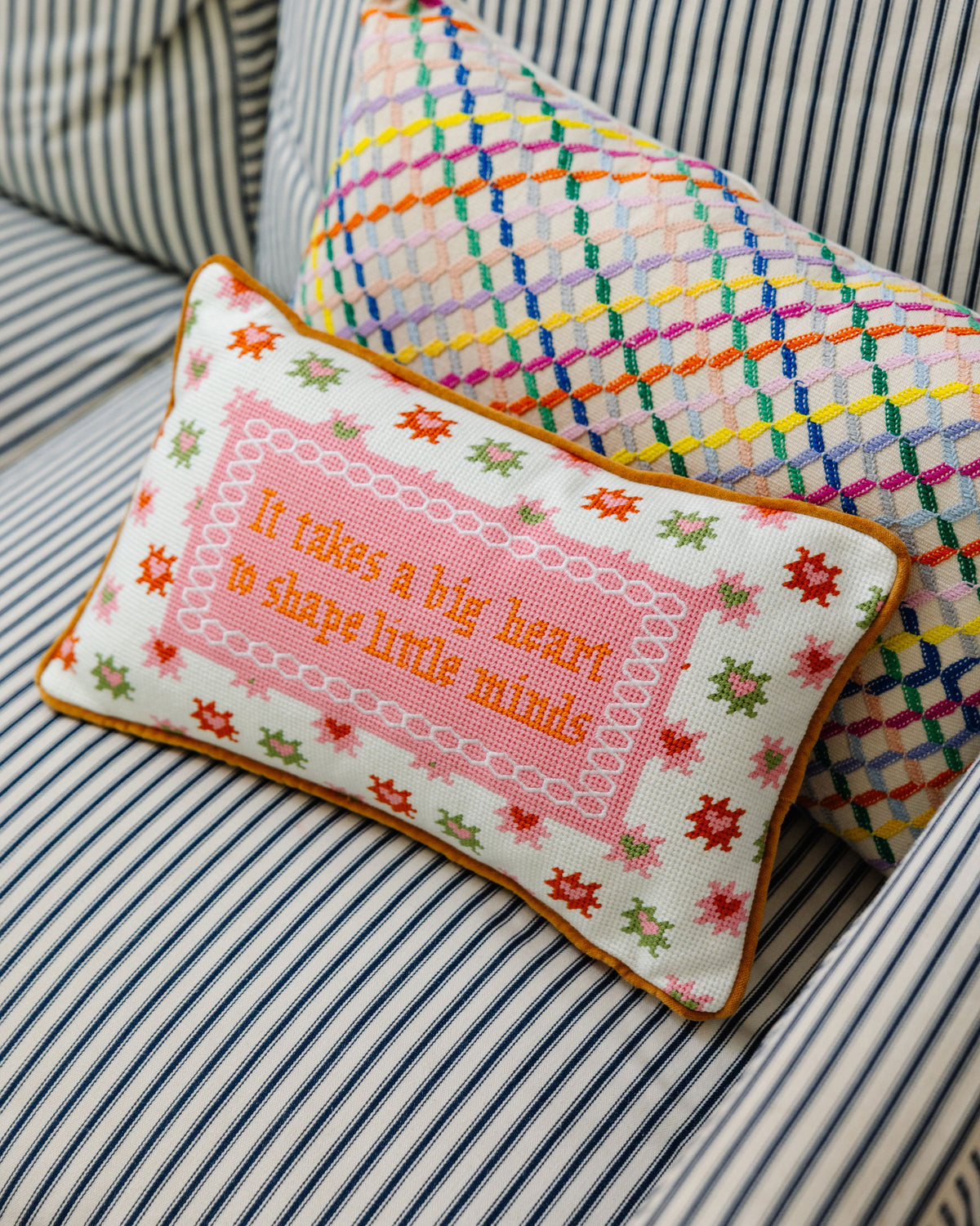 Needlepoint heart slogan throw pillow angled view with pink panel and colorful motifs