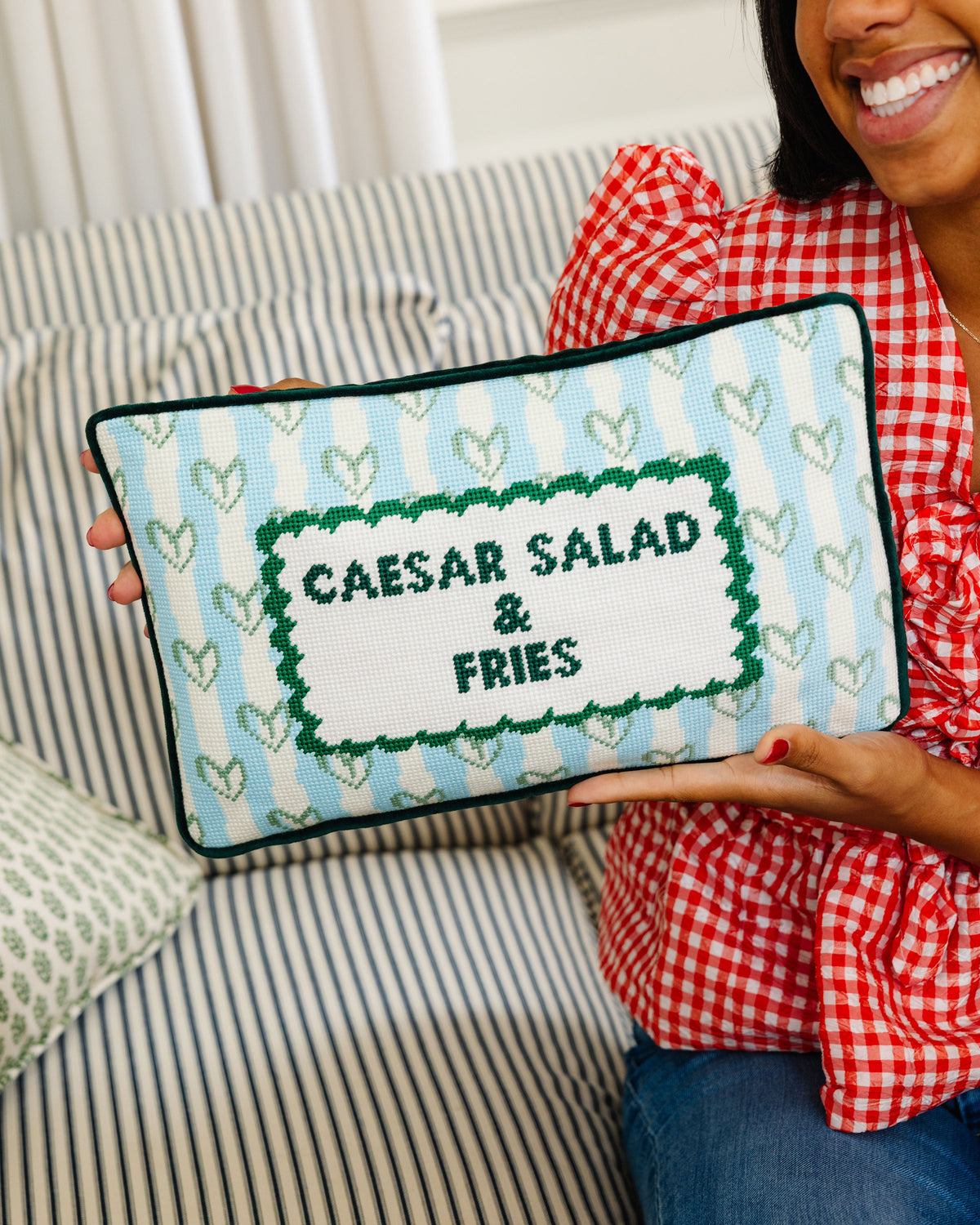 Needlepoint lumbar pillow held in hands with Caesar salad & fries stitched design