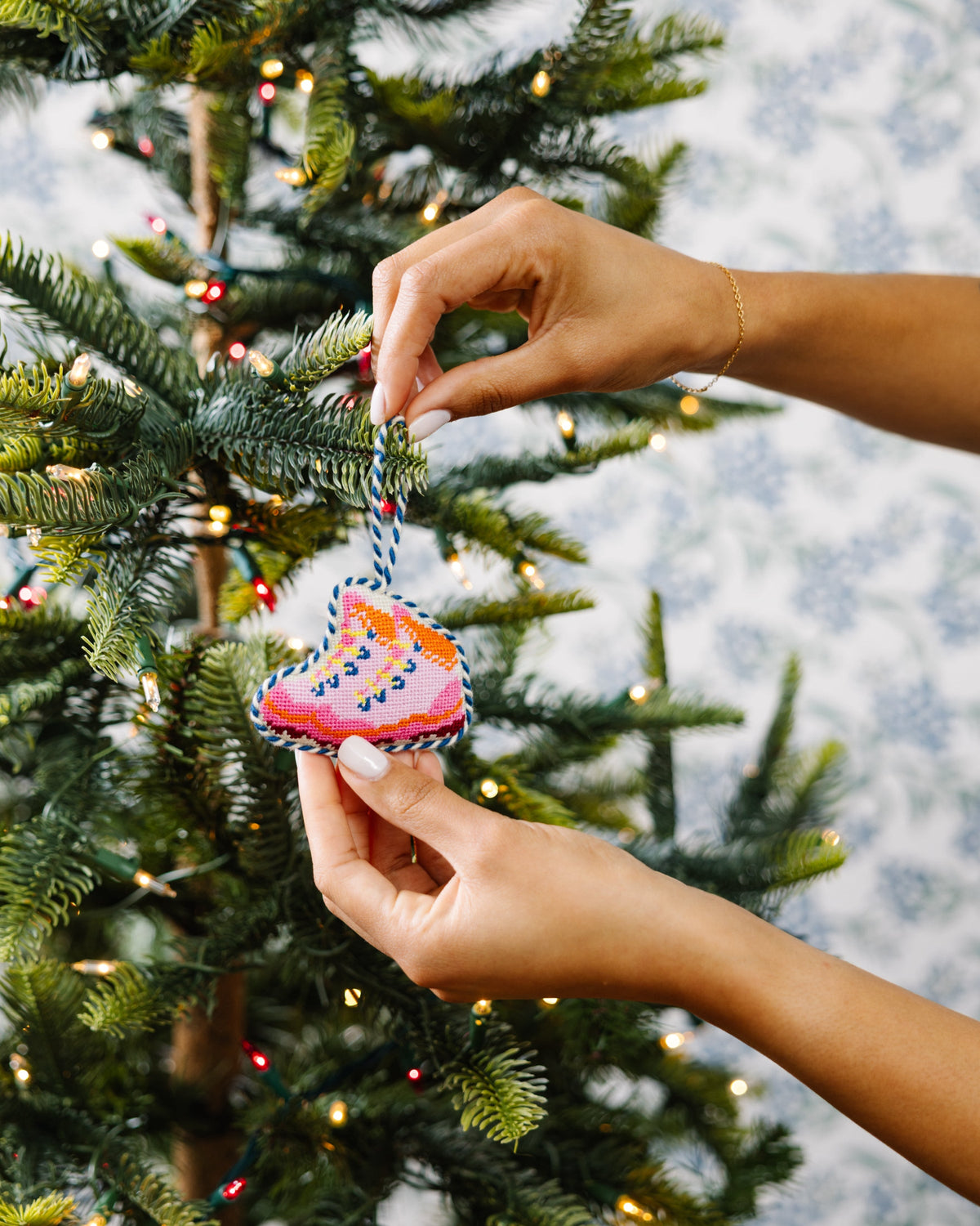 Needlepoint snow boot ornament being placed on a tree branch by hands