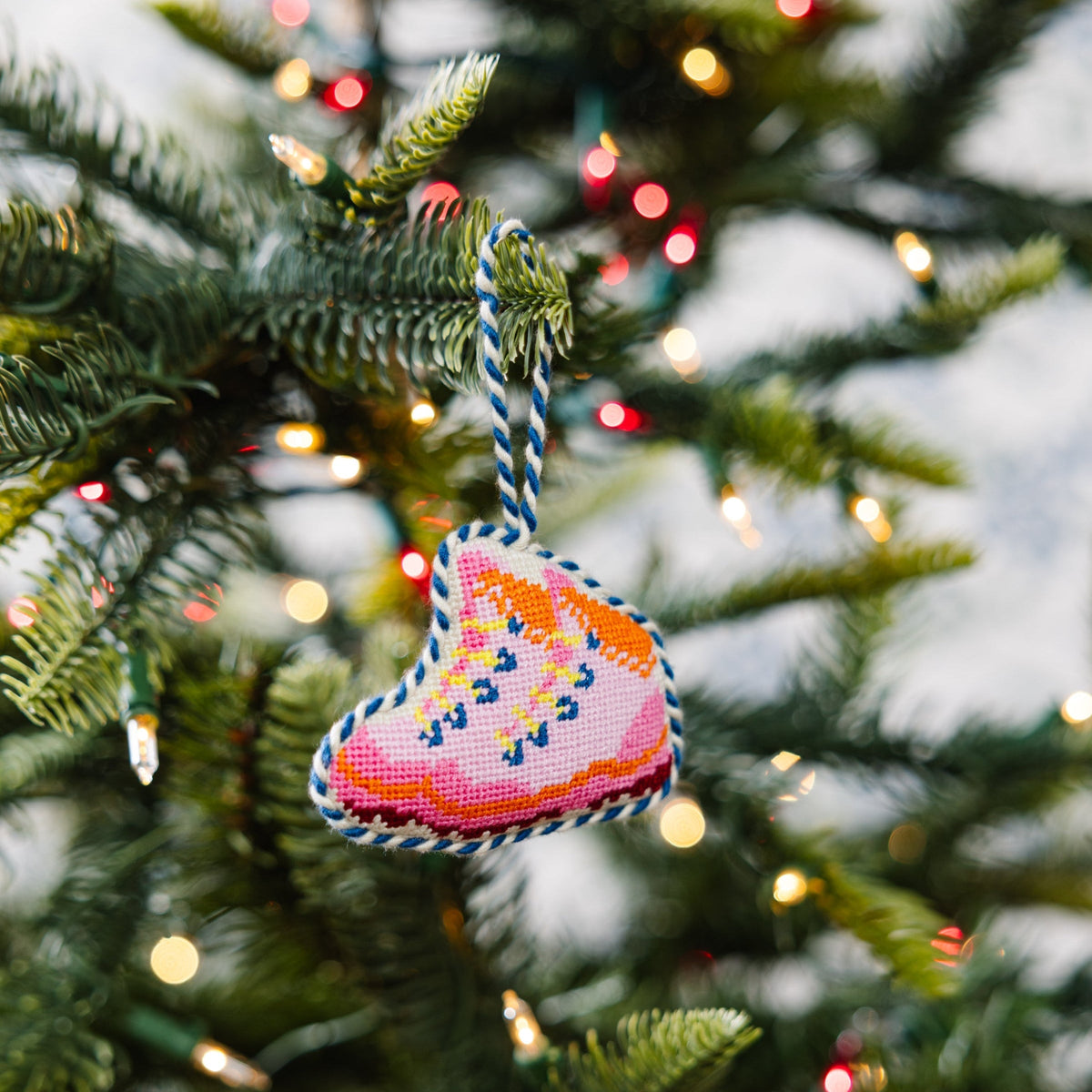 Needlepoint snow boot ornament with colorful stitched pattern hanging from a tree branch