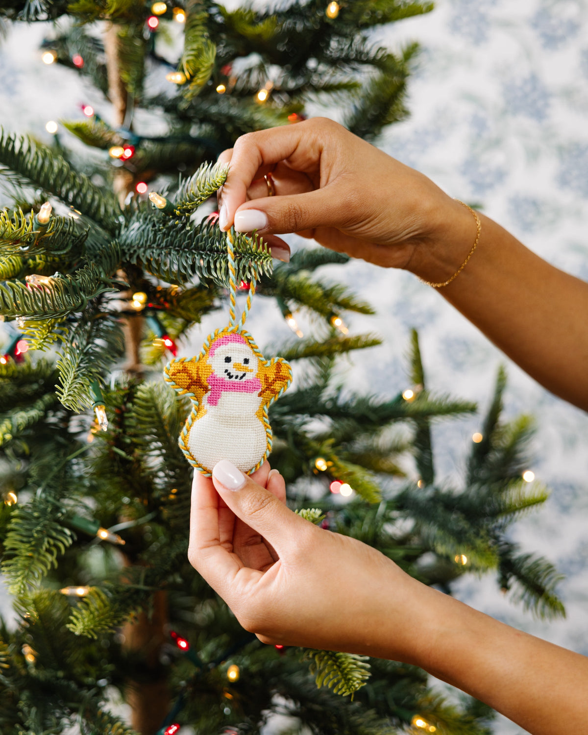 Needlepoint snowman ornament with braided yarn loop, held between hands